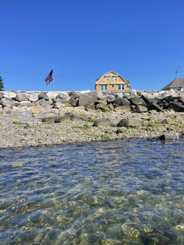 A quaint orange New England cottage overlooks a rocky wall and the ocean.