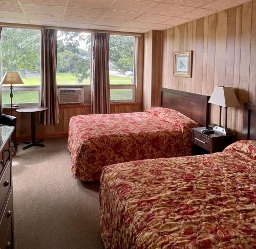 A guest room with two beds and windows overlooking a green lawn and monastery.